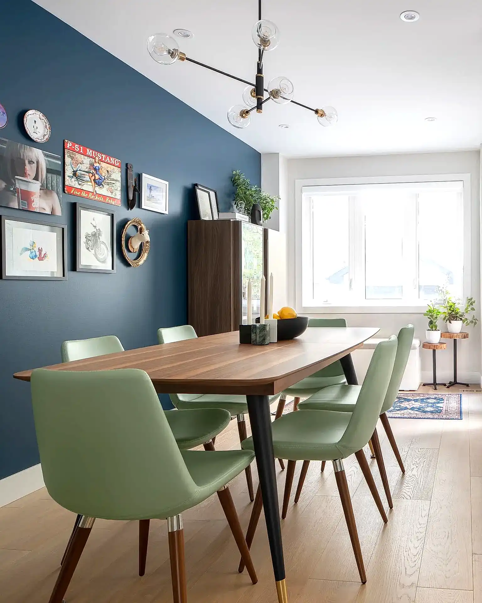 Mid-century modern inspired dining room with wooden table, green chairs and blue accent gallery wall