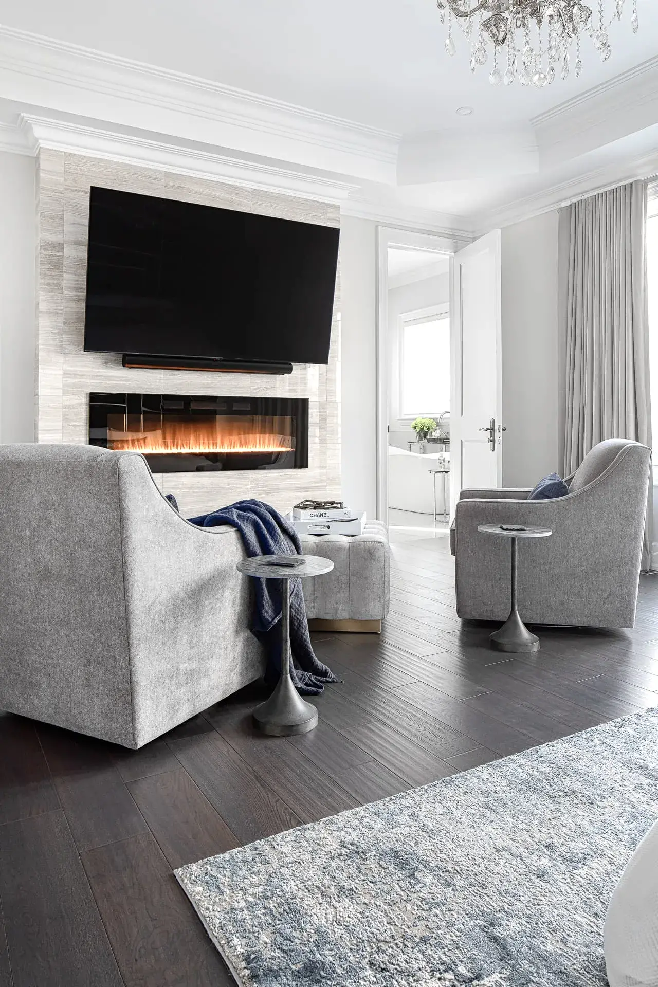 Elegant modern transitional primary bedroom with gray chairs and fireplace feature wall